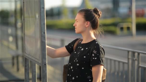 Mujer morena de pie delante de un mapa en la ciudad, chica mirando horario de autobuses y mirando el reloj — Vídeos de Stock