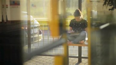 Genç kadın bir Tablet veya ebook bir tren istasyonunda okuma toplu taşıma için otobüs kameradan bekliyor