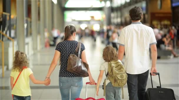 Счастливая семья с маленькой девочкой и мальчиком идет на вокзал, мама с детьми гуляет по аэропорту с чемоданами — стоковое видео