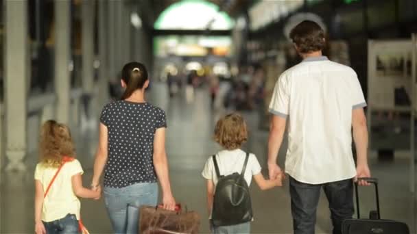 Glückliche Familie mit kleinen Mädchen und Jungen auf dem Weg zum Bahnhof, Mutter Vater und die Kinder laufen mit Koffern durch den Flughafen — Stockvideo