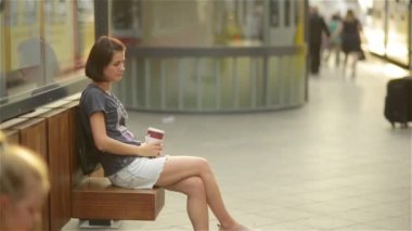 Bir bankta oturan, bir tren bekliyorsun ve içme kahve, kadın genç güzel kız bir plastik şişe çöpe atar