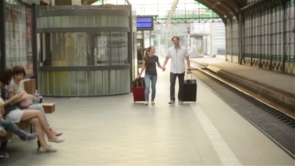 Coppia felice sulla stazione ferroviaria, giovane famiglia che cammina sulla piattaforma ferroviaria, tenendosi per mano — Video Stock