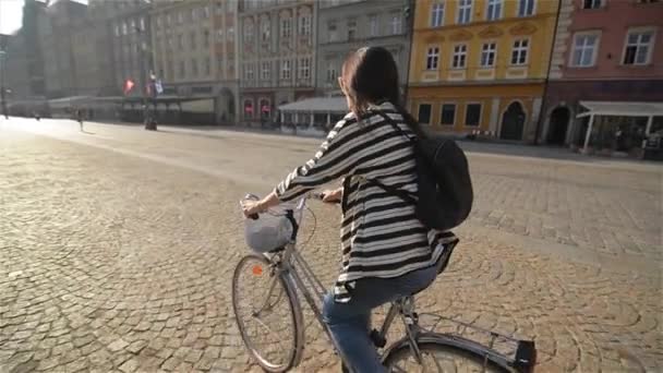 Jonge vrouw een fiets in een stad plein, mooi meisje fietsen op de achtergrond van de straat, oude gebouw — Stockvideo