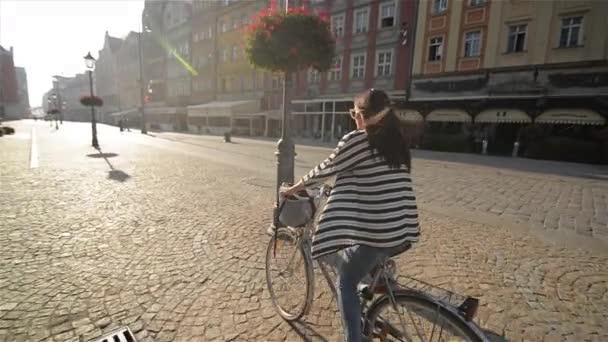 Hermosa joven montando una bicicleta en la ciudad vieja, la luz del sol al aire libre — Vídeo de stock