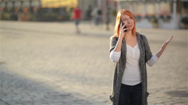 Joven feliz mujer riendo emocionada hablando en el teléfono móvil, chica con el pelo rojo ondea su mano en la calle, fondo urbano de la ciudad . — Vídeos de Stock