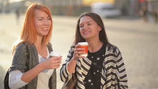 Duas belas meninas elegantes jovens e elegantes se divertindo ao ar livre. Jovens mulheres atraentes bebem café na cidade de verão. Feliz sorrir amigos casal rir da rua, moda jovem — Vídeo de Stock