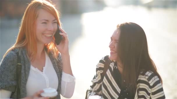 Tjejer går runt i stan på en solig dag med telefoner och dricka kaffe — Stockvideo