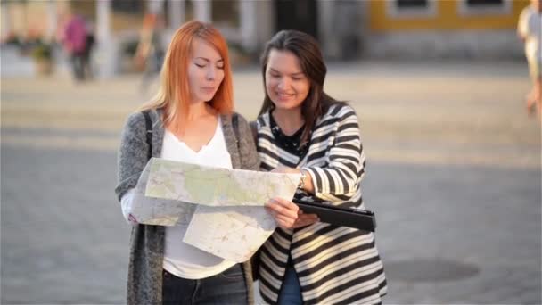 Дві молоді дівчата на вулицях старого міста. Подружки намагаються знайти свій шлях у незнайомому місті. Туристи ретельно розглядають карту району. За ними розташовані прекрасні будівлі . — стокове відео