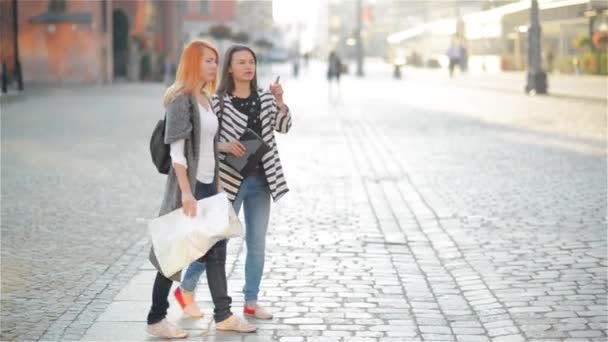 Due giovani ragazze per le strade della città vecchia. Le fidanzate cercano di trovare la loro strada in una città sconosciuta. I turisti considerano attentamente la mappa della zona. Dietro di loro ci sono bellissimi edifici . — Video Stock