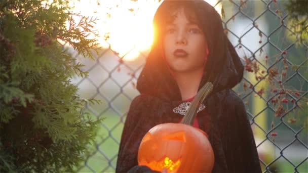Chlapec s dýně oblečený jako upír Halloween party, Dracula drží dýně s hořící svíčkou, pozadí mřížky, venkovní — Stock video