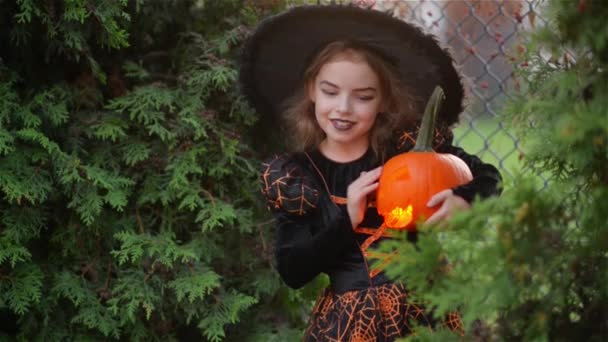 Enfant petite sorcière sur Halloween sur un fond de feuilles d'automne, fille tenant citrouille avec une bougie allumée et l'embrassant — Video