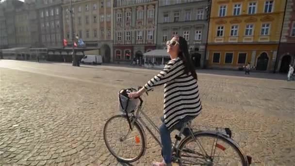 Beautiful young woman smiling while riding her bicycle on a sunny summer day through town in Slow Motion — Stock Video