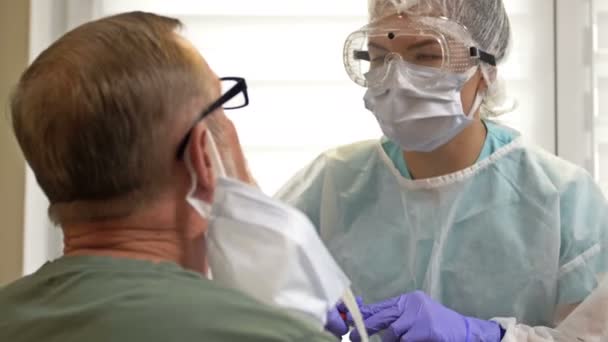 Sjukhusarbetare i skyddsdräkt tar en servett från en äldre patient för coronavirus. — Stockvideo