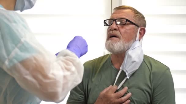 Laboratorietekniker i skyddsdräkt tar en servett från en äldre patient för coronavirus. — Stockvideo