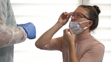 Koruyucu kıyafetli laboratuar teknisyeni, Coronavirus için kadın bir hastadan örnek alıyor..