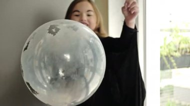 Cadılar Bayramı. Siyah yarasa kostümlü küçük bir kız yarasa şeklinde konfeti dolu bir balonu deliyor. Çocuk çok mutlu..