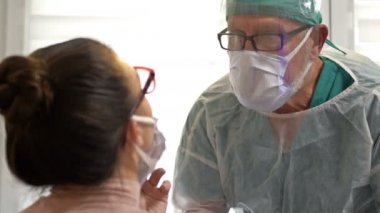 Kadın hasta, koruyucu gözlük ve maske takmış bir sağlık görevlisi tarafından koronavirüs testi yaptırıyor..