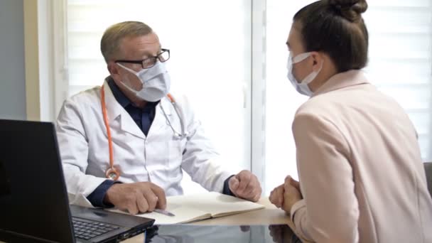 Senior traumatoloog legt röntgenfoto 's uit aan de vrouwelijke patiënt. Dokter en patiënt met medische maskers. Covid-19. — Stockvideo