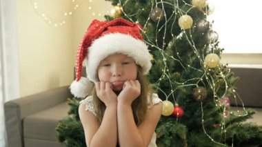 Noel Baba şapkalı üzgün küçük bir kızın portresi bir Noel ağacının arka planında.