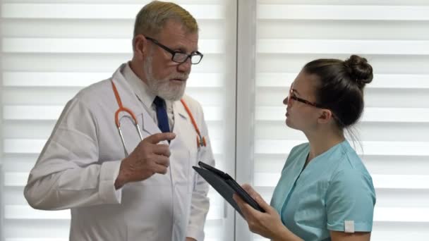 Um médico idoso dá instruções para uma jovem enfermeira. — Vídeo de Stock