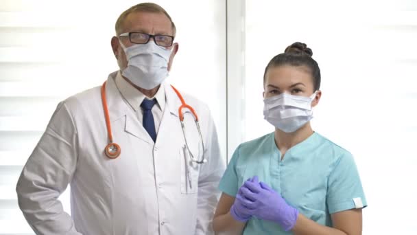 Portrét staršího mužského lékaře a mladé sestry v lékařských maskách ukazující OK. Profesionální tandem. — Stock video