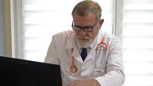 Çevrimiçi doktor. Deneyimli bir doktor dizüstü bilgisayarını kullanan bir hastaya danışır. Covid-19 Salgını. — Stok video