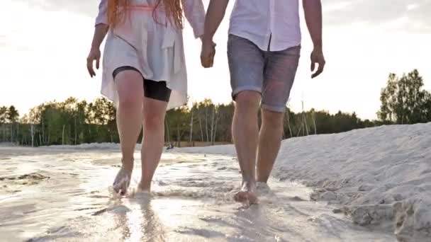 Närbild. Ett romantiskt par går längs stranden vid solnedgången och håller händerna. — Stockvideo