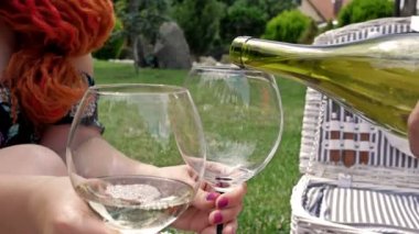 Kadın elinde şişeden beyaz şarap dolduran birinin olduğu iki bardak tutuyor. Yakın plan..