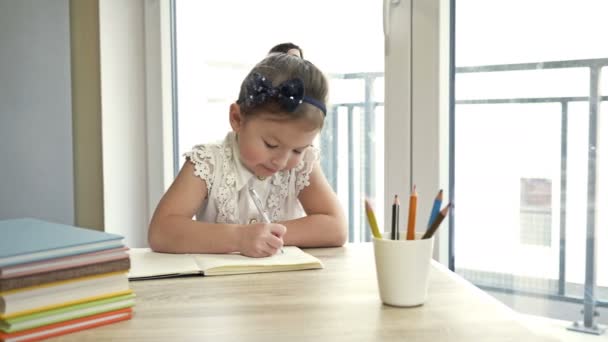 Het kleine schoolmeisje doet haar huiswerk. Schattig kind leert zelf lessen. Terug naar school. — Stockvideo