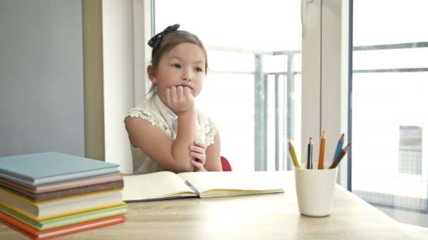 Malá studentka základní školy sedí zamyšleně za stolem a hlavu si opře o ruku. Zpátky do školy. — Stock video