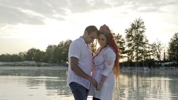 Jezero při západu slunce. Pár milenců stojí ve vodě a drží se za ruce.. — Stock video