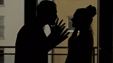 Karanlıkta kavga eden bir çiftin siluetleri bir gece penceresinin arka planında..