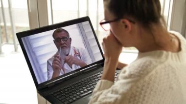 Öksüren genç bir kadın bilgisayarını kullanarak doktoruna danışıyor. Covid-19 salgını sırasında teletıp.