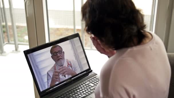 Telemedicina durante la pandemia de Covid-19. Mujer sentada con un portátil en su apartamento consulta a su médico a través de Internet. — Vídeos de Stock