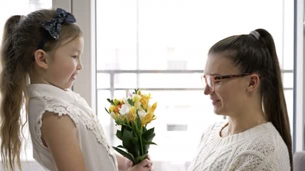 6-7 jaar oud meisje geeft een boeket van freesia 's en knuffelt haar moeder. Moeders Verjaardag of Moederdag. — Stockvideo