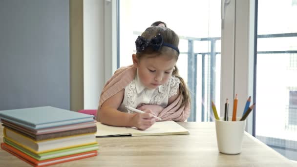 Een klein basisschoolmeisje die huiswerk maakt. Schattig kind leert alleen. Terug naar school. — Stockvideo