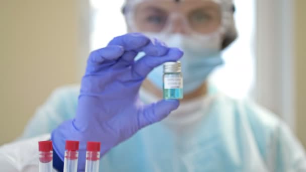 Professional female scientist wearing glasses and a mask holds a 2019-ncov coronavirus vaccine sample in her hand. Stop the pandemic. — Stock Video