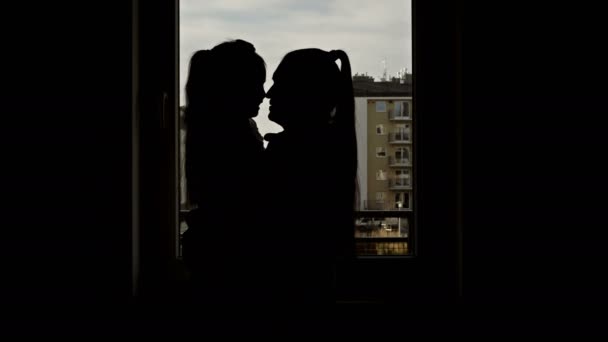 Silhuett av en kvinna med en liten dotter i sina armar mot bakgrund av en natt fönster. — Stockvideo