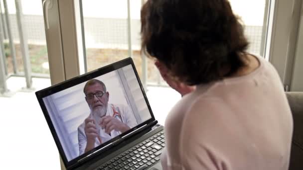Telemedycyna podczas pandemii Covid-19. Kobieta siedząca z laptopem w mieszkaniu konsultuje się z lekarzem przez Internet. — Wideo stockowe
