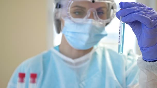 한 전문가는 깨끗 한 실험실에서 보호용 양복, 장갑, 고글, 마스크를 갖춘 19 종의 코로나 바이러스 백신에 대한 연구를 하고 있다. — 비디오