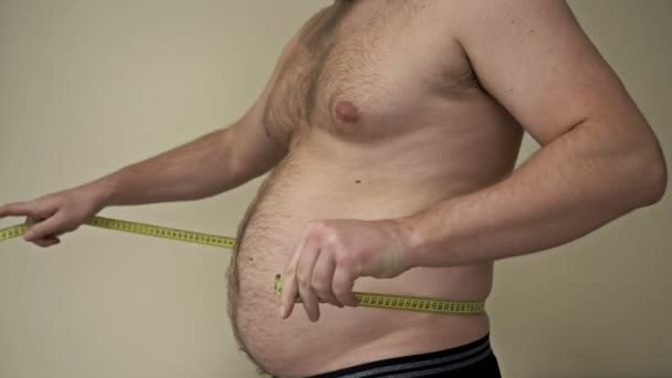 Fat man measures his waist circumference with a tape measure and shows the folds of excess fat on his stomach. Overweight problem. — Stock Video