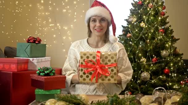 Egy bájos játékos nő portréja, aki karácsonyi ajándékokat készít a szeretteinek. A karácsonyfa hátterében. — Stock videók