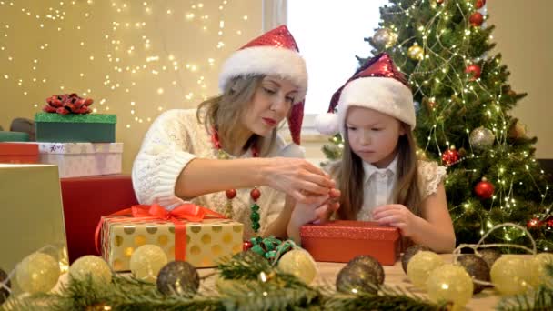 Mamma e la sua figlioletta in cappelli di Babbo Natale stanno amorevolmente preparando regali per i propri cari sullo sfondo di un albero di Natale. L'umore festivo. Buon Natale. Ciao.. — Video Stock