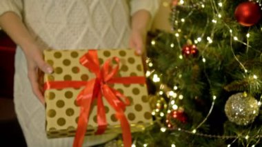 Kadınların elleri çok güzel paketlenmiş bir hediyeyi uzatıyor. Noel ağacının arka planında. - Mutlu yıllar. Mutlu Noeller..