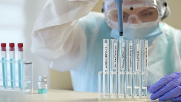 Científica profesional en gafas protectoras y mascarilla haciendo experimento con reactivos en laboratorio. Creación de una vacuna contra el coronavirus. — Vídeo de stock