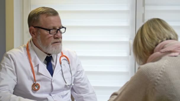 En äldre, erfaren manlig läkare bedömer symtomen på en patientsjukdom. Kvinnan hostar.. — Stockvideo