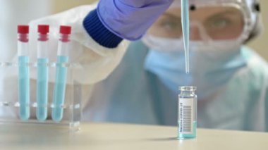 Koruyucu gözlüklü ve maskeli profesyonel kadın bilim adamı laboratuvarda reaktörlerle deney yapıyor. Koronavirüse karşı aşı üretimi.