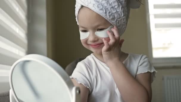 Menina 6-7 anos com um olhar sério aplica manchas sob os olhos na frente do espelho. Copia sua mãe. — Vídeo de Stock