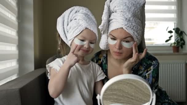 Die junge Frau und ihre kleine Tochter machen nach der Dusche Schönheitsbehandlungen. Beide genießen es, sich selbst im Spiegel zu betrachten. — Stockvideo