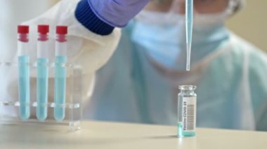 Koruyucu gözlüklü ve maskeli profesyonel kadın bilim adamı laboratuvarda reaktörlerle deney yapıyor. Koronavirüse karşı aşı üretimi.